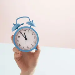 En hand håller en blå väckarklocka. Snart är det dags för antagningsbesked gymnasiet!