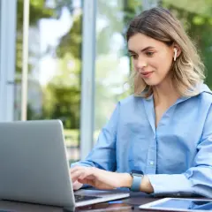 Kvinna med hörlurar arbetar på laptop utomhus, drömmer om bra betalda jobb utan utbildning.
