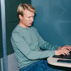 Man i ljudisolerad bås jobbar intensivt på laptop, kanske funderar på konsekvenserna av illojalitet mot arbetsgivare och skadestånd.