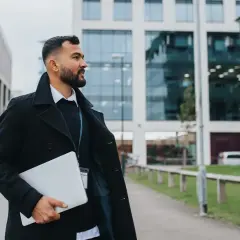 Man med laptop går förbi moderna kontorsbyggnader, redo att plugga logistik.