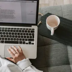 Person som arbetar med e-learning på en laptop i soffan, med en kaffekopp bredvid.
