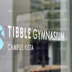 Tibble Gymnasium, Campus Kista. En blå logotyp och vit text på en glasdörr.