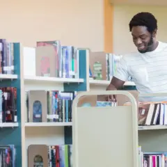 Man med bokvagn i bibliotek, kanske på väg att sortera böcker som en del av sin bibliotekarie utbildning.