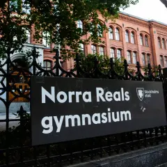 Skylt med texten "Norra Reals gymnasium" framför en vacker tegelbyggnad.
