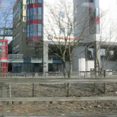 Modern byggnader med glasfasader och en röd, cylindrisk hiss. Skylten "Kunskapsgymnasiet Globen" syns på en av byggnaderna.
