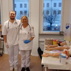 Två glada medarbetare från Medlearn AB i en övningssal med medicinsk utrustning.