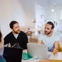 Män och kvinnor diskuterar webbutveckling utbildning vid laptops i ett ljust kontorslandskap.