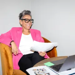 En leende logistik konsult i rosa kavaj sitter med papper och laptop.