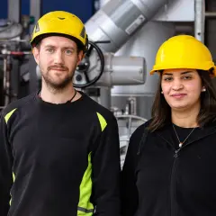 Två personer med gula hjälmar står framför industriell utrustning. De är studenter vid byggbranschens utbildningscenter.