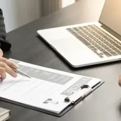 Intervju pågår. En person pekar på ett CV medan en annan lyssnar. En laptop ligger på bordet, redo för digitala cady utbildningar.