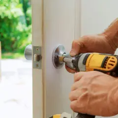 En person skruvar i ett dörrhandtag med en skruvdragare. Detta är en del av låssmed utbildning för att lära sig montera och reparera lås.
