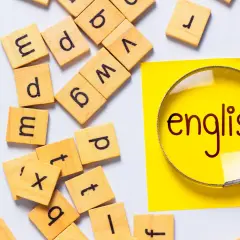 Förstoringsglas över ordet "english" på en gul post-it, omgivet av bokstavsbrickor. Perfekt för engelska 6 distans.