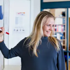 Glad kvinna med blondt hår skriver på en whiteboard. Hon kanske studerar socialpedagog utbildning distans.