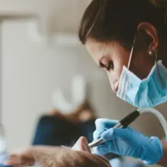 En tandhygienist i mask och handskar arbetar med en patient. En del av tandhygienist utbildning.