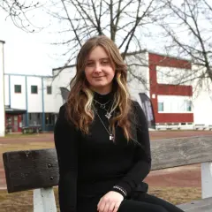 Ung kvinna sitter på en bänk utanför en skolbyggnad. Hon hoppas på ett stipendium för gymnasiet.