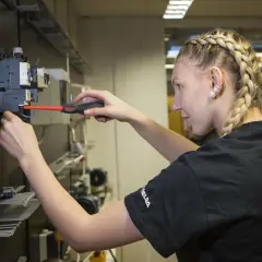 En ung kvinna med flätat hår arbetar med elinstallationer, en framtida elektriker från gymnasiet.