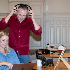 Man med hörlurar och kvinna vid laptop, en hundstatyett på bordet. De arbetar med sitt it konsult-projekt.