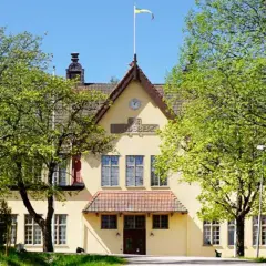 Gult hus med flagga på taket, omgivet av gröna träd. En annons för internat i Sverige.