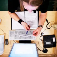 Person vid skrivbord med dator, telefon och papper. Kanske arbetar med lagen om distansavtal.