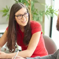 En kvinna med glasögon och en röd tröja deltar i en hr business partner utbildning. Hon lyssnar uppmärksamt på en kollega.