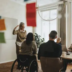 En social media manager presenterar idéer för sitt team. En kvinna i rullstol deltar i mötet.