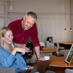 En it-specialist hjälper en kollega med en laptop. De skrattar tillsammans i en ljus lokal.