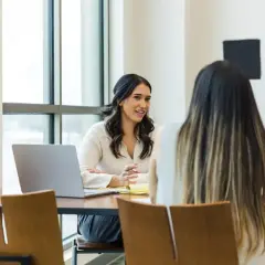 Två kvinnor sitter vid ett bord, en med laptop. Kanske diskuterar de kurator utbildning distans.