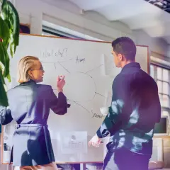 Kvinnlig och manlig kollega diskuterar på whiteboard, en del av en cloud engineer utbildning.