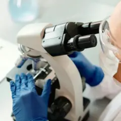 En forensiker arbetar med ett mikroskop i ett laboratorium. En laptop syns i bakgrunden.