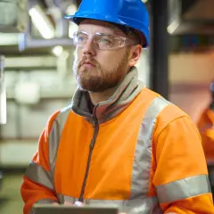 Man i blå hjälm och varselkläder vid kontrollpanel. En del av en produktionstekniker utbildning.