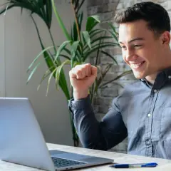 Ung man jublar framför sin laptop, kanske har han hittat roliga jobb eller lyckats med ett projekt.