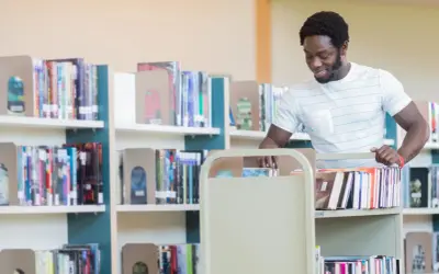 Man med bokvagn i bibliotek, kanske på väg att sortera böcker som en del av sin bibliotekarie utbildning.