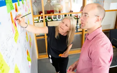 En ux designer pekar på en whiteboard med post-it-lappar.