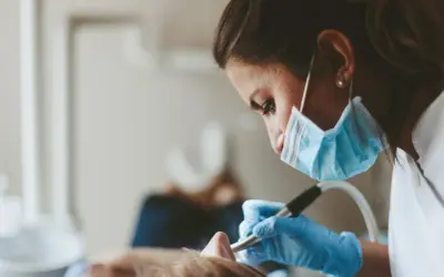 En tandhygienist i mask och handskar arbetar med en patient. En del av tandhygienist utbildning.