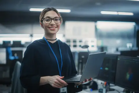 En kvinna med glasögon håller en laptop i ett modernt kontor, redo för sin cyber security utbildning distans.