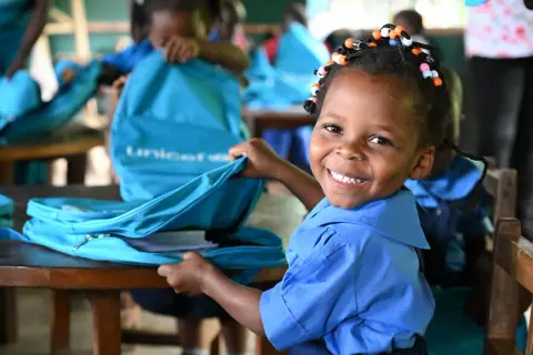 Glad flicka i blå skoluniform öppnar en UNICEF-väska i en skola.