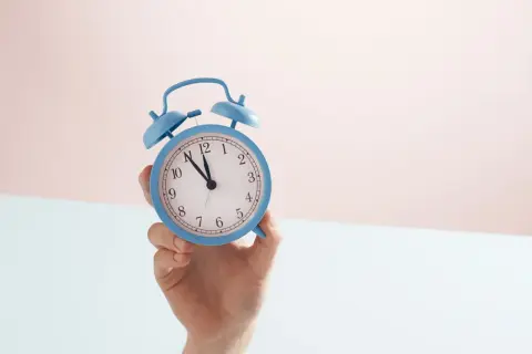 En hand håller en blå väckarklocka. Snart är det dags för antagningsbesked gymnasiet!