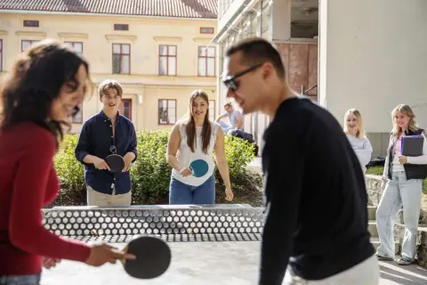 Elever spelar pingis utomhus vid Falu Frigymnasium. Soligt och glada miner bland ungdomarna.