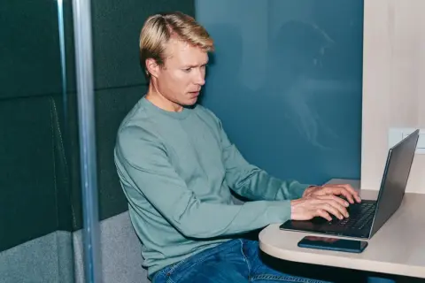 Man i ljudisolerad bås jobbar intensivt på laptop, kanske funderar på konsekvenserna av illojalitet mot arbetsgivare och skadestånd.