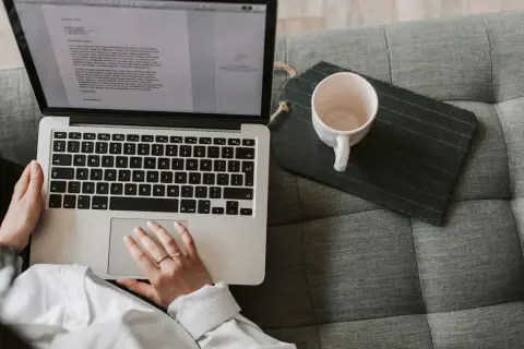 Person som arbetar med e-learning på en laptop i soffan, med en kaffekopp bredvid.