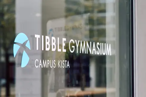Tibble Gymnasium, Campus Kista. En blå logotyp och vit text på en glasdörr.