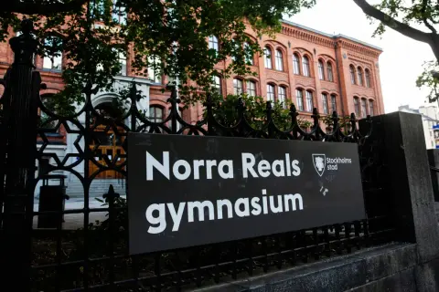 Skylt med texten "Norra Reals gymnasium" framför en vacker tegelbyggnad.