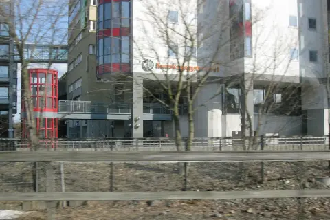 Modern byggnader med glasfasader och en röd, cylindrisk hiss. Skylten "Kunskapsgymnasiet Globen" syns på en av byggnaderna.