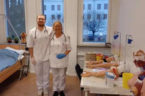 Två glada medarbetare från Medlearn AB i en övningssal med medicinsk utrustning.