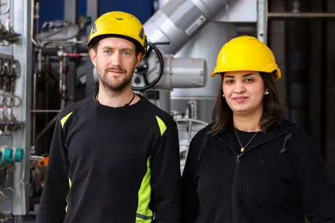 Två personer med gula hjälmar står framför industriell utrustning. De är studenter vid byggbranschens utbildningscenter.