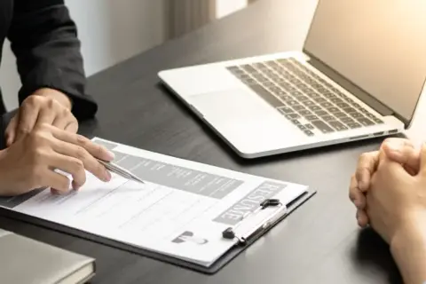 Intervju pågår. En person pekar på ett CV medan en annan lyssnar. En laptop ligger på bordet, redo för digitala cady utbildningar.