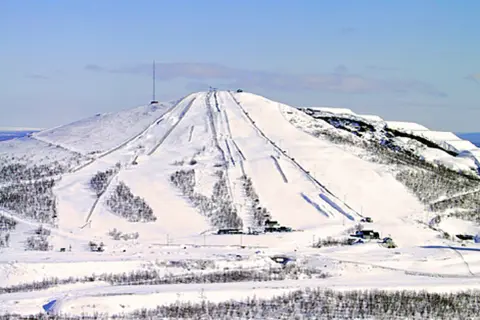 Snöklädda pister på ett berg med en mast på toppen, en vy som påminner om rymdgymnasiet Kiruna.