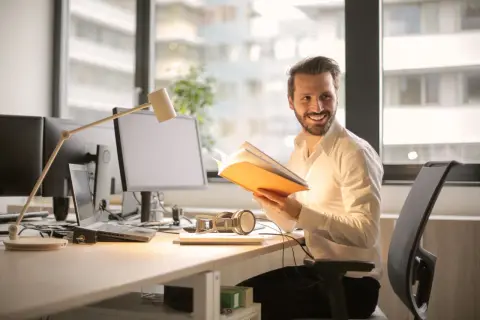 Man vid skrivbordet med bok, kanske ett av de där konstiga jobben där man läser istället för att jobba.