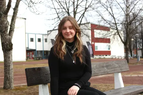 Ung kvinna sitter på en bänk utanför en skolbyggnad. Hon hoppas på ett stipendium för gymnasiet.