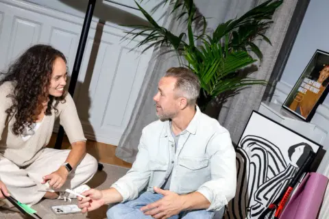 Två personer diskuterar en digital strateg. En kvinna med lockigt hår och en man med grått hår sitter på golvet.